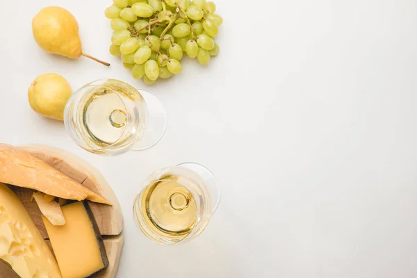 Top view of different types of cheese on wooden board, wine glasses and fruits on white — Stock Photo