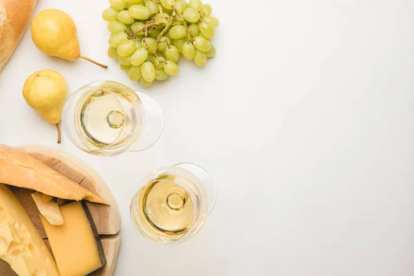 Top view of different types of cheese on wooden board, wineglasses and fruits on white — Stock Photo