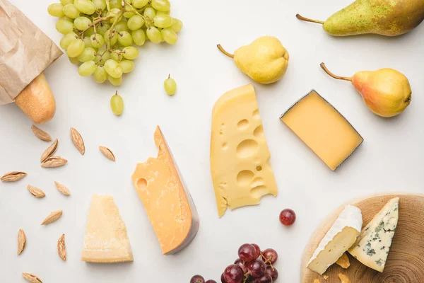 Draufsicht auf verschiedene Käsesorten, Trauben, Birnen, Mandeln und Baguette auf Weiß — Stockfoto