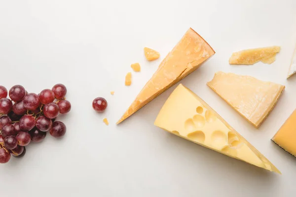 Vista superior de diferentes tipos de queso y uvas sobre blanco - foto de stock