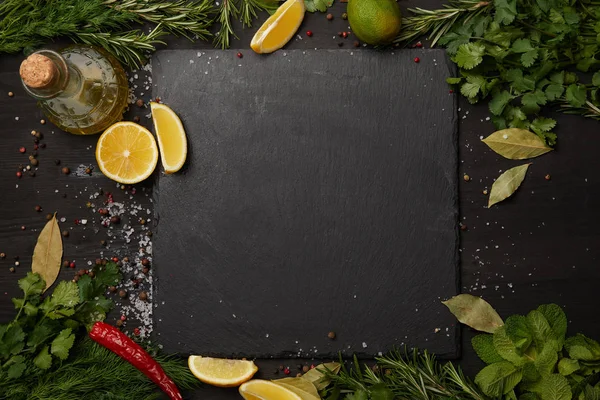 Tavola di ardesia nera con erbe fresche e fette di limone con olio d'oliva — Foto stock