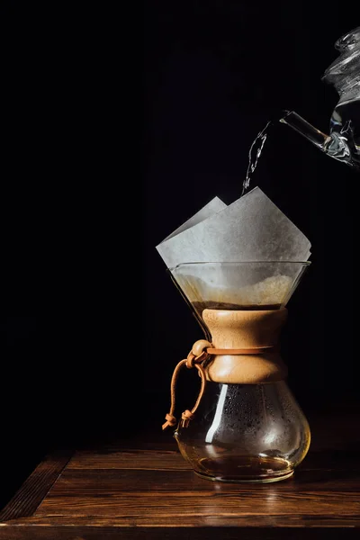 Agua caliente que vierte en chemex con el cono del filtro en la tabla de madera - foto de stock