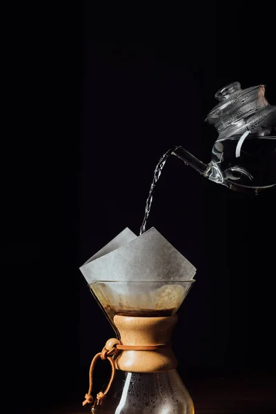 Agua caliente que vierte en chemex con el cono del filtro, aislado en negro - foto de stock