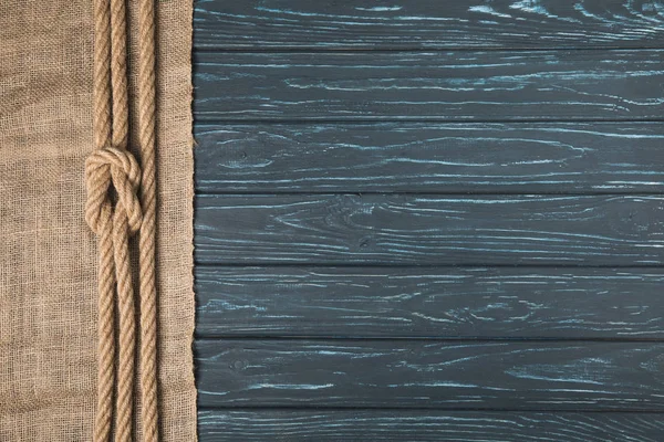 Vista superior de cuerda náutica marrón anudada sobre tela de saco sobre superficie de madera — Stock Photo