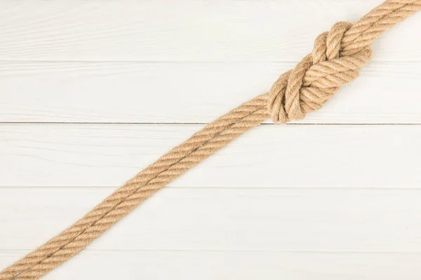 Вид сверху на коричневую морскую верёвку с узлом на белой деревянной поверхности — стоковое фото