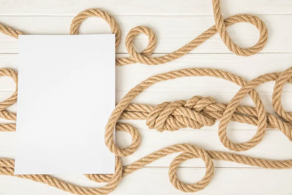 Top view of empty paper on brown nautical knotted ropes on white wooden surface — Stock Photo