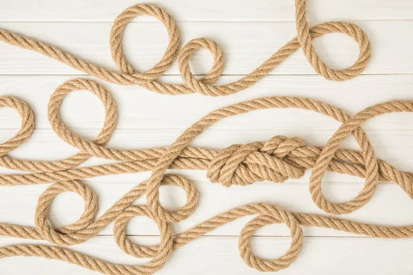 Vue de dessus des cordes nautiques marron nouées sur la surface en bois blanc — Photo de stock