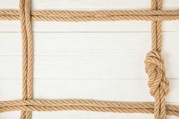 Vista superior da moldura feita por cordas náuticas marrons com nó no fundo de madeira branco — Fotografia de Stock
