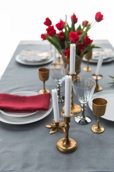 Selective focus of candles in vintage candle holders, bouquet of red tulips and arranged empty plates on tabletop — Stock Photo