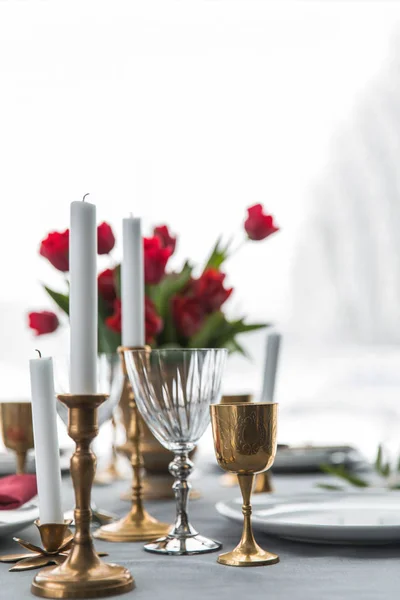 Selective focus of candles in vintage candle holders, bouquet of red tulips and arranged empty plates on tabletop — Stock Photo