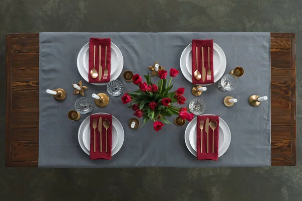 Draufsicht auf rustikale Tischdekoration mit rotem Tulpenstrauß, angelaufenem Besteck, Weingläsern, Kerzen und leeren Tellern auf der Tischplatte — Stockfoto