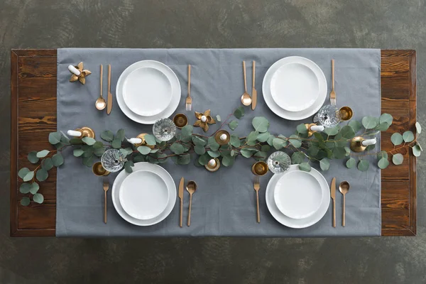 Vue du dessus de la table rustique avec eucalyptus, couverts ternis, verres à vin, bougies et assiettes vides sur la table — Photo de stock