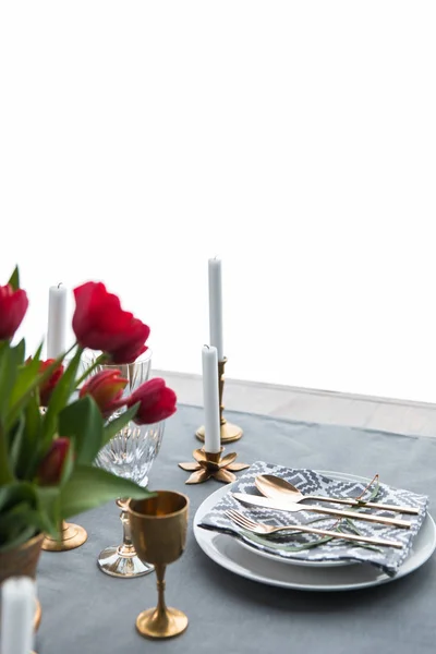 Close up view of rustic table arrangement with red tulips, empty wine glasses, vintage silverware and plates — Stock Photo