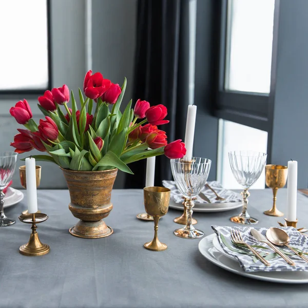 Close up view of bouquet of red tulips on tabletop with arranged vintage cutlery and candles — Stock Photo