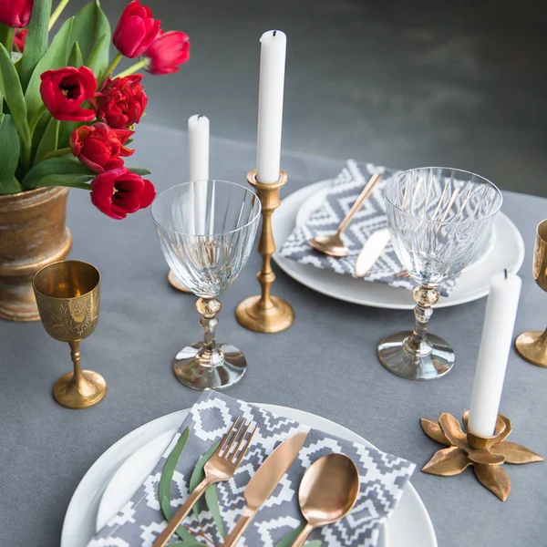 Close up view of rustic table arrangement with red tulips, empty wine glasses, vintage silverware and plates — Stock Photo