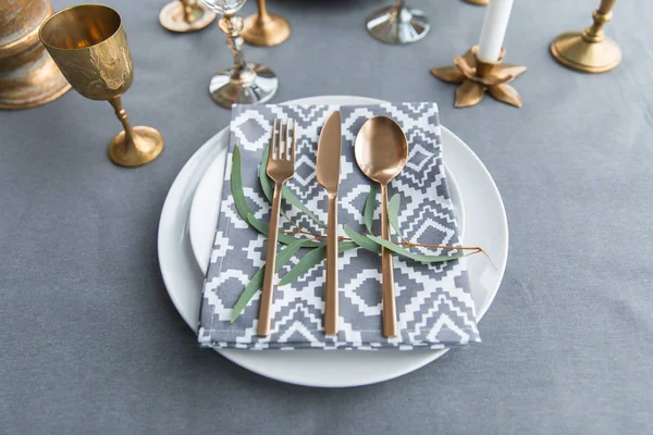 Close up view of rustic table setting with vintage tarnished silverware, napkin on plates, green plant and wine glasses — Stock Photo