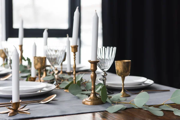 Tavolo rustico con eucalipto, posate vintage, candele in portacandele e piatti vuoti — Foto stock