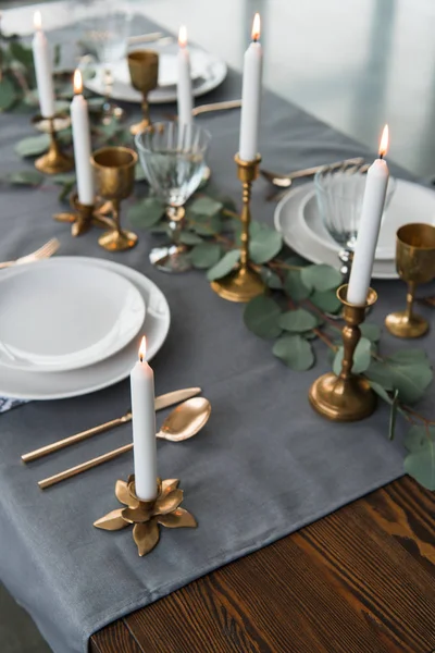 Vista de cerca del arreglo de mesa rústico con eucalipto, cubiertos vintage, velas en candelabros y platos vacíos - foto de stock