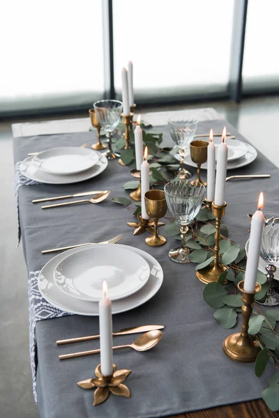 Close up view of rustic table arrangement with eucalyptus, vintage cutlery, candles in candle holders and empty plates — Stock Photo
