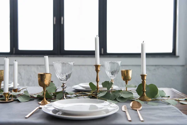 Close up view of rustic table arrangement with eucalyptus, tarnished cutlery, candles in candle holders and empty plates — Stock Photo