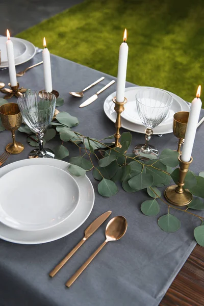 Close up view of rustic table setting with eucalyptus, vintage tarnished cutlery, candles in candle holders and empty plates — Stock Photo