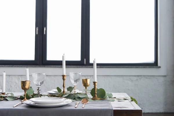 Vue rapprochée de la disposition rustique de la table avec eucalyptus, couverts vintage ternis, bougies dans des bougeoirs et des assiettes vides — Photo de stock