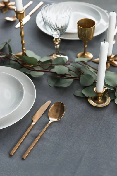 Close up view of rustic table arrangement with eucalyptus, vintage cutlery, candles in candle holders and empty plates — Stock Photo