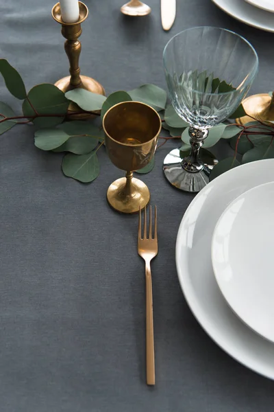 Vue rapprochée de la disposition rustique de la table avec winecups, eucalyptus, couverts vintage, bougies dans des bougeoirs et des assiettes vides — Photo de stock