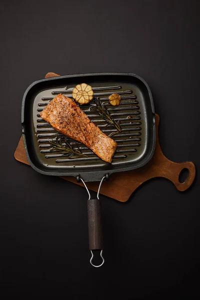 Top view of arranged grilled salmon steak with rosemary on wooden cutting board on black tabletop — Stock Photo