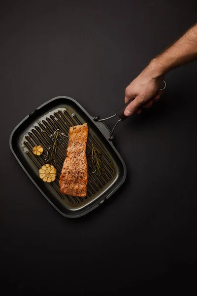 Обрізаний знімок людини, що тримає гриль зі стейком лосося на чорній стільниці — стокове фото