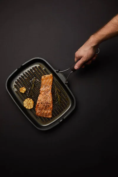 Plan recadré d'un homme tenant un gril avec un steak de saumon sur une table noire — Photo de stock