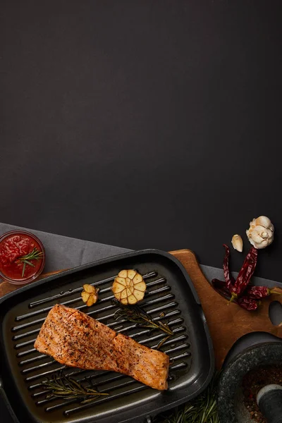 Top view of arranged grilled salmon steak on wooden cutting board, ingredients and sauce on black tabletop — Stock Photo