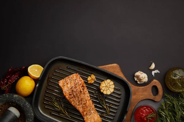 Top view of arranged grilled salmon steak on wooden cutting board, sauce, ingredients and cutlery on black tabletop — Stock Photo