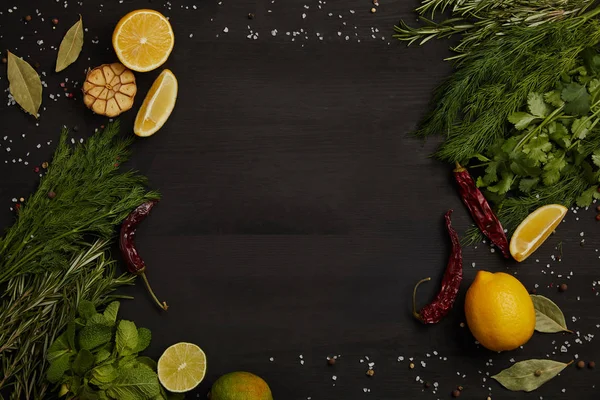 Flat lay with citrus fruits, chili peppers, bay leaves, spices, rosemary and parsley on black surface — Stock Photo