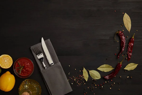Plat avec couverts, sauce, piments, épices et morceaux de citron sur la table noire — Photo de stock