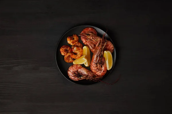 Top view of grilled shrimps and lemon pieces on plate on black surface — Stock Photo