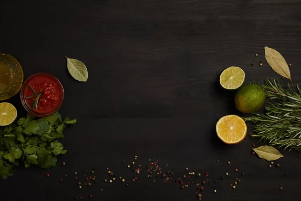 Flat lay with sauce, citrus fruits pieces, spices, parsley and rosemary on black surface — Stock Photo