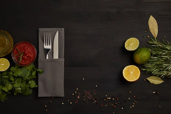 Flache Lage mit Besteck, Sauce, Rosmarin, Gewürzen und Zitrusfruchtstücken auf schwarzer Tischplatte — Stockfoto