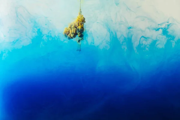 Крупним планом вид змішування синіх, бірюзових і жовтих фарб бризки у воді — стокове фото