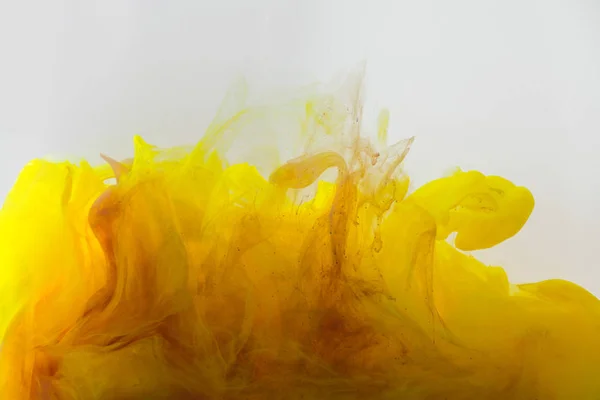 Vista de cerca de la mezcla de tintas amarillas y marrones salpicaduras en agua aislada en gris - foto de stock