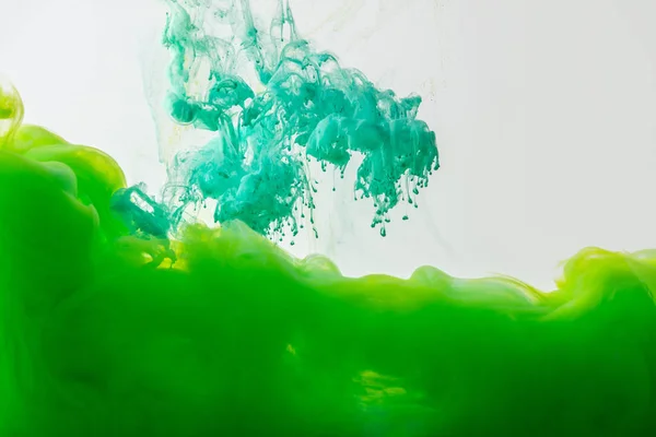 Vista de cerca de la mezcla de pinturas turquesas verdes y brillantes salpicaduras en agua aislada en gris - foto de stock