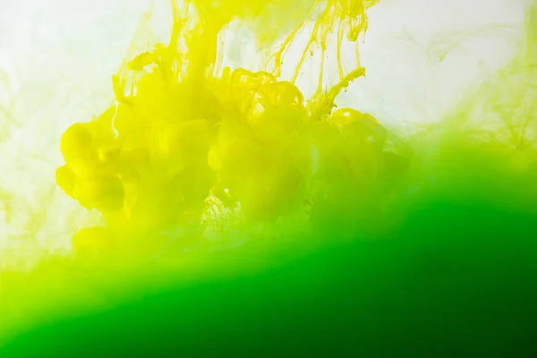 Close up view of mixing of green and yellow inks splashes in water isolated on gray — Stock Photo