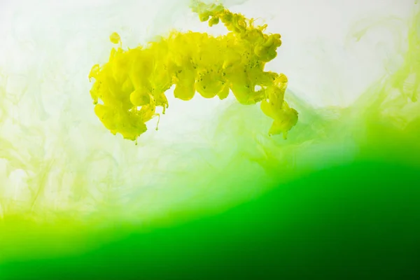 Close up view of mixing of green and yellow paints splashes in water isolated on gray — Stock Photo