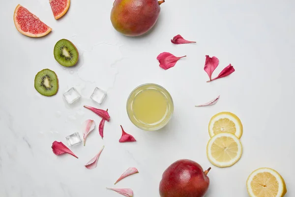 Posa piatta con cocktail alcolici, cubetti di ghiaccio, frutta esotica disposti e petali di fiori sulla superficie bianca — Foto stock