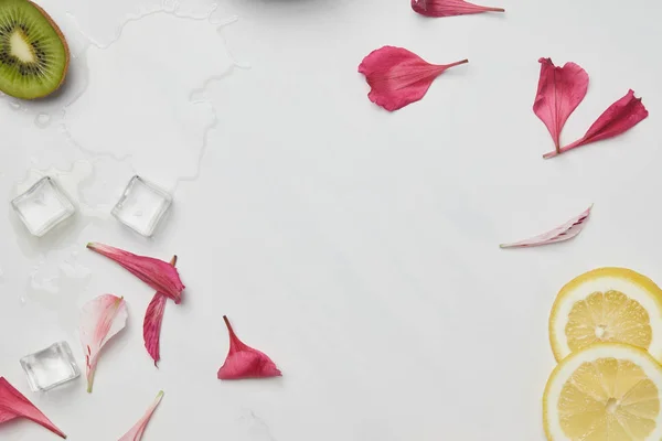 Flat lay with flower petals, ice cubes, lemon and kiwi pieces on white tabletop — Stock Photo