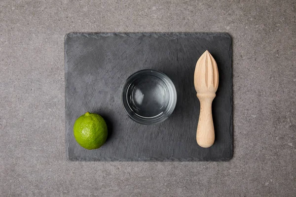 Flat lay with wooden squeezer, fresh lime and empty glass on grey surface — Stock Photo