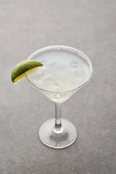 Vista de cerca del cóctel de alcohol con trozo de lima y hielo en la superficie gris - foto de stock