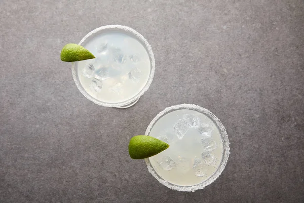 Vue de dessus des cocktails de margarita à l'alcool froid avec des morceaux de citron vert sur la table grise — Photo de stock