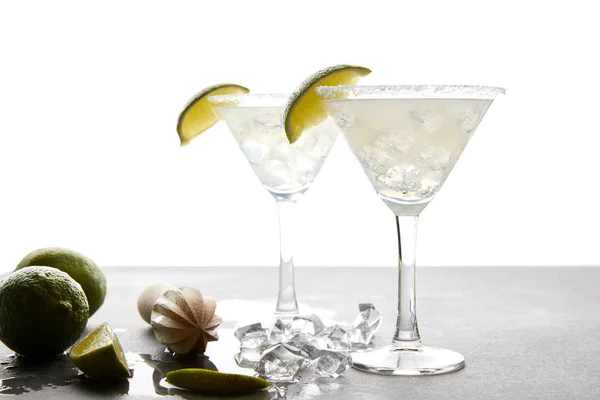 Vue rapprochée des cocktails margarita avec des morceaux de lime et un pressoir en bois sur la surface grise sur blanc — Photo de stock