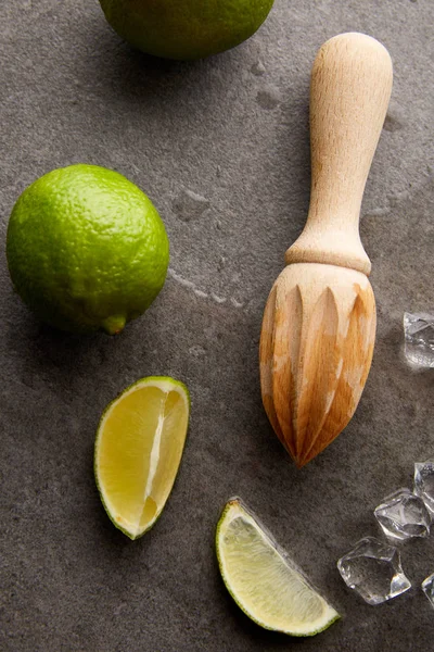 Draufsicht auf Holzpresse, Limetten und Eiswürfel für Cocktails auf grauer Oberfläche — Stockfoto